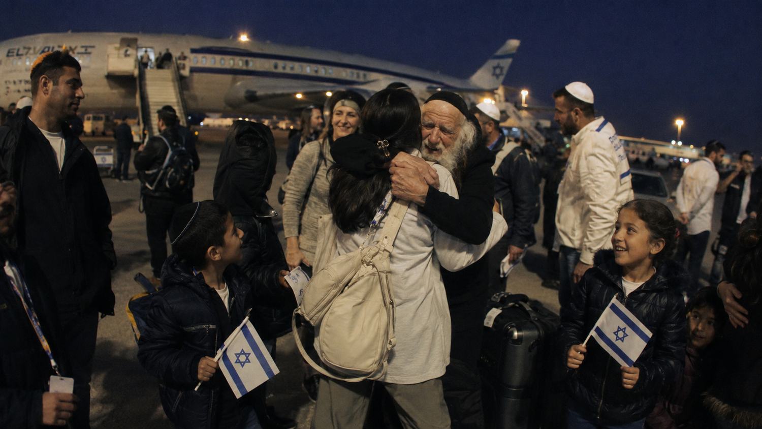 New immigrants embracing on the tarmac beside an El Al aircraft, children holding Israeli flags